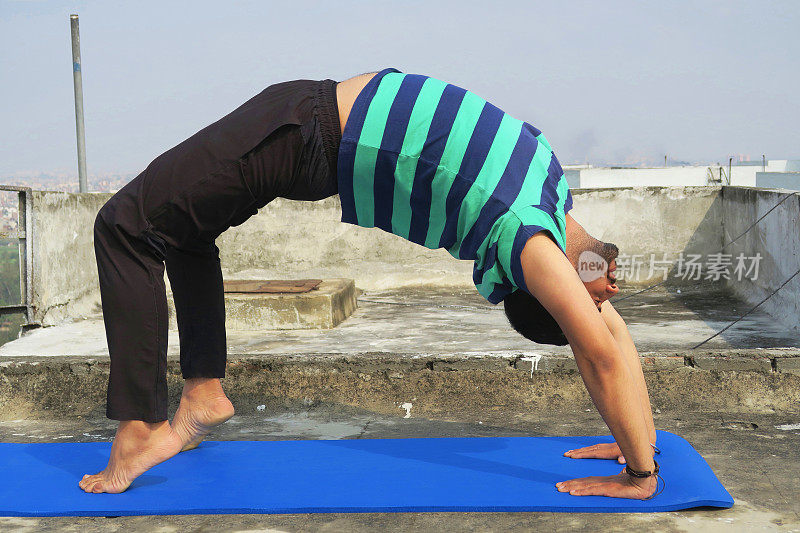 印度男子在屋顶上练习向上的弓/轮(Urdhva Dhanurasana)瑜伽姿势，德里，印度